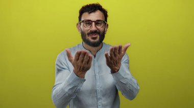 Sakallı ve gözlüklü İspanyol bir adam kameraya doğru elleriyle bir öpücük yolluyor. Parlak sarı arka plana karşı. Sevgisini ve çekiciliğini oyuncu bir hareketle ifade ediyor..