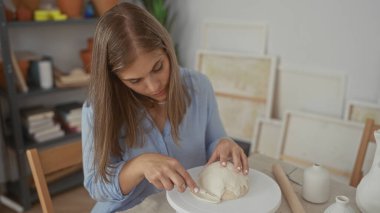 Genç sarışın kadın özenle çömlek kil kubbesini şekillendirir parmakları stüdyoda döner döner döner tablonun üzerinde; yaratıcılık tutkusu dinginliğe odaklanır.