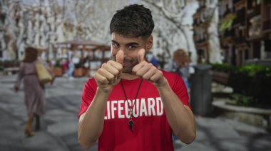 Kırmızı tişörtlü adam şehirde gündüz vakti sokakta baş parmak işareti yapıyor; güven onayı.