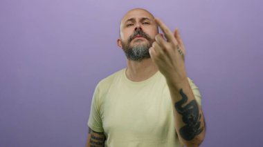 Kel, beyaz, sakallı, parmakları mor arka planda gezen, sıradan gömlekli, kolunda dövmesi olan, izole edilmiş, ciddi bir yüz ifadesi olan bir adam..