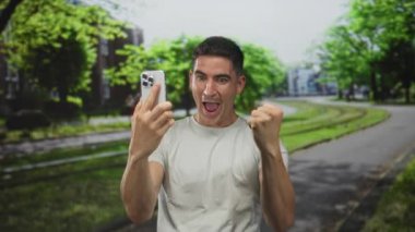 Genç İspanyol adam gülümseyen ve yürüyen tramvay raylarının yakınındaki yeşil park yolunda telefonu kulağına tutuyor..