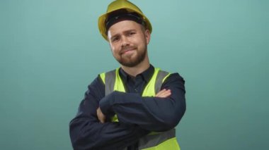 Stüdyoda kolları çaprazlanmış sarı kasklı ve yansıtıcı yelek giyen bir adam; güven becerisi profesyonelliği.