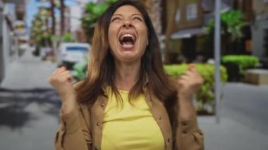 İspanyol orta yaşlı kadın, güneşli şehir caddesinde bulanık vitrinler ve saksı çalıları arasında el çırptı; neşe.