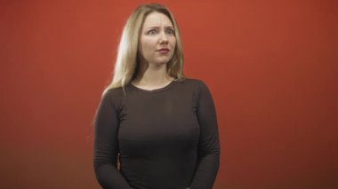 Kadın sinagoga parmağıyla dokunur ve stüdyoda kırmızı arka plan ve düz ışıklandırma ile asabi bir surat asar;.