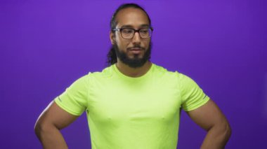 Neon yeşil gömlekli ve gözlüklü bir adam, stüdyoda kollarını gösteren kalçalı bir adam..