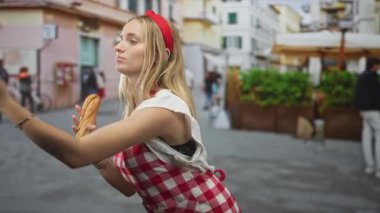 Kırmızı elbiseli kadın şef elinde bir ekmek tutuyor ve kolunu sokak pazarında kaldırıyor..