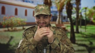 Askeri kamuflaj üniformalı asker yeşil bir parkta ellerini sımsıkı tutuyor..