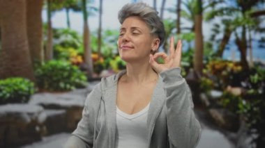 Kadın yeşil orman yeşilliklerinde gülümserken işaret parmağıyla 