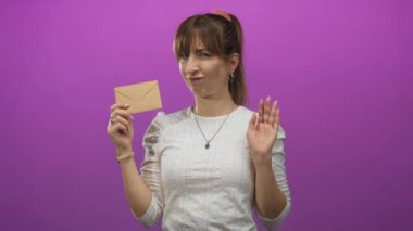 Genç beyaz kadın elinde küçük bir zarf tutuyor ve mor stüdyoda avuç içi hareketi sergiliyor..