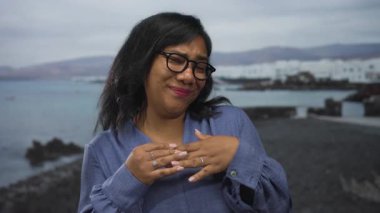 Afrika kökenli Amerikalı gözlüklü ve mavi bluzlu bir kadın kayalık bir sahil sahilinde el ele tutuşuyor..