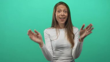 Bir kadın el çırpıyor ve camgöbeği stüdyosunda yüzüne yakın avuçlarını tutuyor uzun kollu beyaz bir bluz giyiyor, kameraya bakıyor..