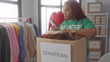 Yeşil gönüllü gömleği giyen bir kadın, kapalı bir bağış merkezinde elleri ile katlanmış süveterler düzenliyor; cömertlik.