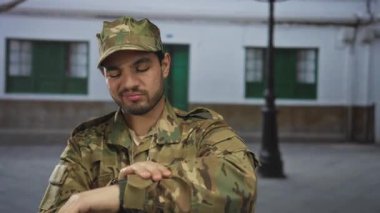 Kamuflaj üniformalı asker, bir sokak lambası altında boş bir eski kasaba caddesinde dururken bileğinde nöbet tutuyor; disiplin görevi.