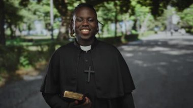 İncil 'i elinde tutan rahip parkta papazlık tasması ve haç takıyor, inanç neşeye ulaşır..