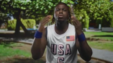 Adam el çırpıyor ve Sunny Park 'ta gülümsüyor ABD basketbol forması ve mavi bileklik takıyor; sevinç kutlaması gururu.