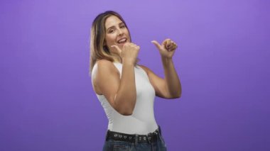 Kadın başparmağıyla göğsünü işaret ederken stüdyoda başparmağı mor arka planla ısırıyor; oyuncu özgüven.