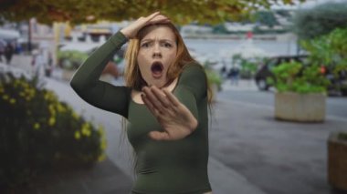 Kızıl saçlı kadın, avuç içi avuçlarını açık bir şekilde elinde savunma jesti ile sokakta durmak için uzatıyor; alarm savunması..