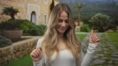 Yeşil park avlusunda çıplak elle dans eden kadın, palmiye ağaçları arasında taş patika boyunca; mutluluk özgürlüğü mutluluğu.