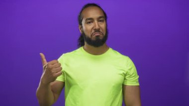 Stüdyoda, mor arka planda, neon yeşil gömlekli, parmaklarını kaldırmış bir adam görülüyor; şüphecilik..