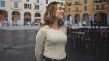 Kadın başını arkaya eğip yukarı bakıyor, nazikçe gülümsüyor. Plazada yüzünü gösteriyor. Huzur yansıması..