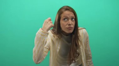 Öne eğilip dikkatle dinlerken yeşil stüdyoda elini kulağına götüren Latin asıllı genç bir kadın..