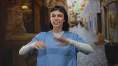 Mavi önlüklü kadın hemşire, dil uzatıyor ve güneş ışığında kaldırılan kaldırımda el kaldırıyor..