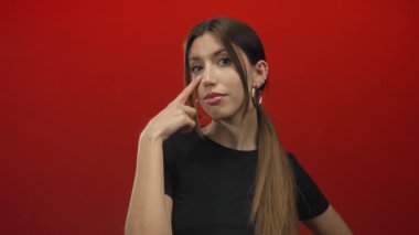 Stüdyoda kırmızı arka plan, halka küpeler ve siyah kapak takan kadınlar göz göze gelir..