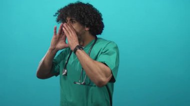 Steteskop ve kıvırcık saçlı yeşil önlüklü bir adam tıbbi uyarı için deniz mavisi stüdyoda bağıracak..