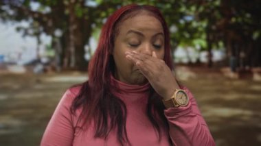 Pembe bluz giyen kadın, yeşil parktaki kötü kokuya karşı burnunu çimdikliyor. Ağaç tepe örtüsü olan kadın iğrenme reaksiyonu rahatsızlığı..