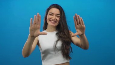 Kadın, elleri stüdyoda mavi bir zemin ile bir çerçeve jesti yapar; yaratıcılık hayal gücü oyunculuğu.