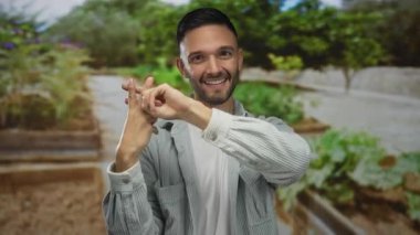 Genç adam yemyeşil ve doğal güzelliklerle çevrili bir hashtag jesti yaparak, yemyeşil bir bahçede gülümsüyor, neşe ve doğa ile bağını somutlaştırıyor..
