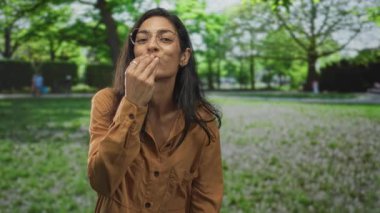 Kadın ağızdan ağıza öpüşüyor ağaçlar ve çimlerle temizleniyor, gözlük takıyor ve kahverengi gömlek giyiyor, gözleri kapalı ve gülümsüyor;.