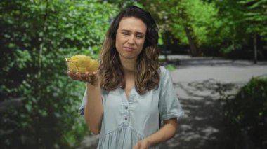 Açık yeşil bir parkta açık camdan patates cipsi tutan İspanyol kadın. Dudakları büzüşmüş. Şüphecilik şüphe uyandırıcı..