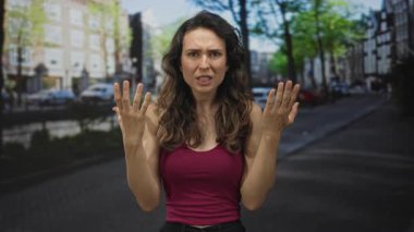 Genç İspanyol kadın, güneşli kanal caddesinde, binanın ön cephesinin altında çıplak kollarını silkiyor..