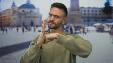 Genç İspanyol asıllı bir adam, Vatikan 'da savaş jesti yapıyor, ünlü simgelerin bulanık arka planıyla duruyor, yüzleşme havasını ve kültürel zenginliği aktarıyor..