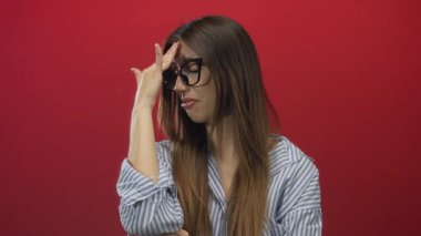Gözlüklü genç İspanyol kadın kırmızı stüdyoda çıplak elle alnına dokunuyor. Stres bunalımı..