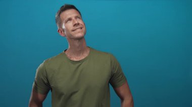 Stüdyoda boynu görünen zeytin tişörtü giyen ve tepe örtüsüne gülümseyen bir adam. Düşünceli bir yansıma..