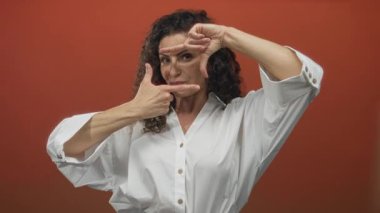 Turuncu stüdyoda beyaz gömlekli genç kadın yüz ve parmak çerçeveli jest; yaratıcılık vizyonu.