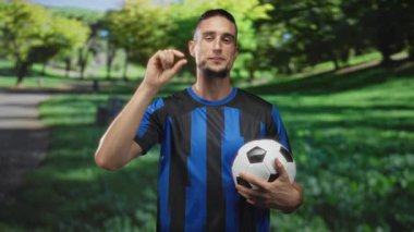 Yeşil çizgili, patikalı ve ağaçlı bir parkta mavi çizgili bir forma giyerken göz göze sokulacak ve çimdikleyecek bir adam..