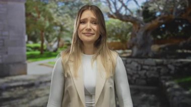 Açık havada duygularını ifade eden bir kadın güneşli bir parkta ellerini kaldırmış yemyeşil ve ağaçlarla çevrili..