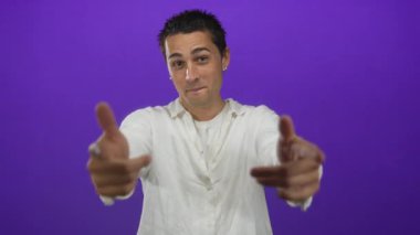 İzole edilmiş mor arka plana karşı el kol hareketi yapan genç bir İspanyol, stüdyo ortamında beyaz gömlek ve küpeler giyiyor.