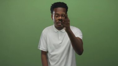 Yeşil stüdyoda gözlüklü genç adam doğrudan göz teması kurarak işaret ediyor..