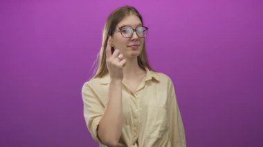 Sarışın kadın mor stüdyo ortamında hafif bir gülümsemeyle yuvarlak gözlükleri ayarlıyor..
