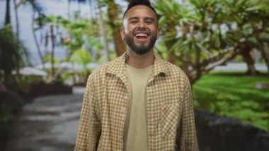 Dili açık gülümseyen ve parkta iki eliyle kaya boynuzlarını gösteren adam damalı bej gömlek giyiyor; eğlenceli rock gençliği.