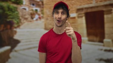 Eski şehir caddesinde elleri çenesinde kırmızı şapkalı ve kırmızı tişörtlü genç adam; tefekkür.