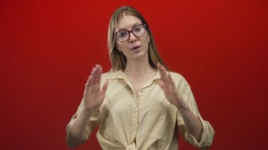 Kadın açık avuçlarla meditasyon yapıyor canlı kırmızı stüdyo arkaplanına karşı jest yapıyor; sakinlik.