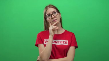 Kırmızı gönüllü gömlekli sarışın, gözlüklü, elleri çenesinde, stüdyoda yeşil arka planda olan sarışın kadın..