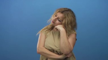 Mavi stüdyoda çıplak koluyla uzanan genç sarışın kadın, gözleri kapalı ve düşünceli duruş; düşünceli sakin duruş.