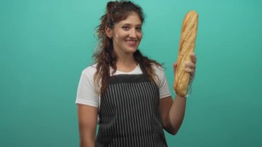 Elinde uzun bir baget tutan ve tek kullanımlık eldiven ve çizgili önlük giyerken ekmeği gösteren bir kadın..