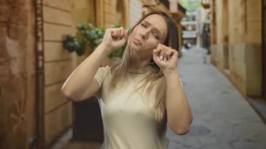 Sarışın bir kadın şakacı bir şekilde şehir sokaklarında ağlar gibi yapıyor, açık havada neşeli duygular sergiliyor..
